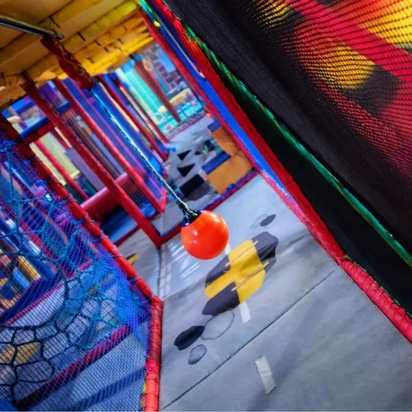 Red ball suspended in colourful inflatable play structure with netting and padded walls.