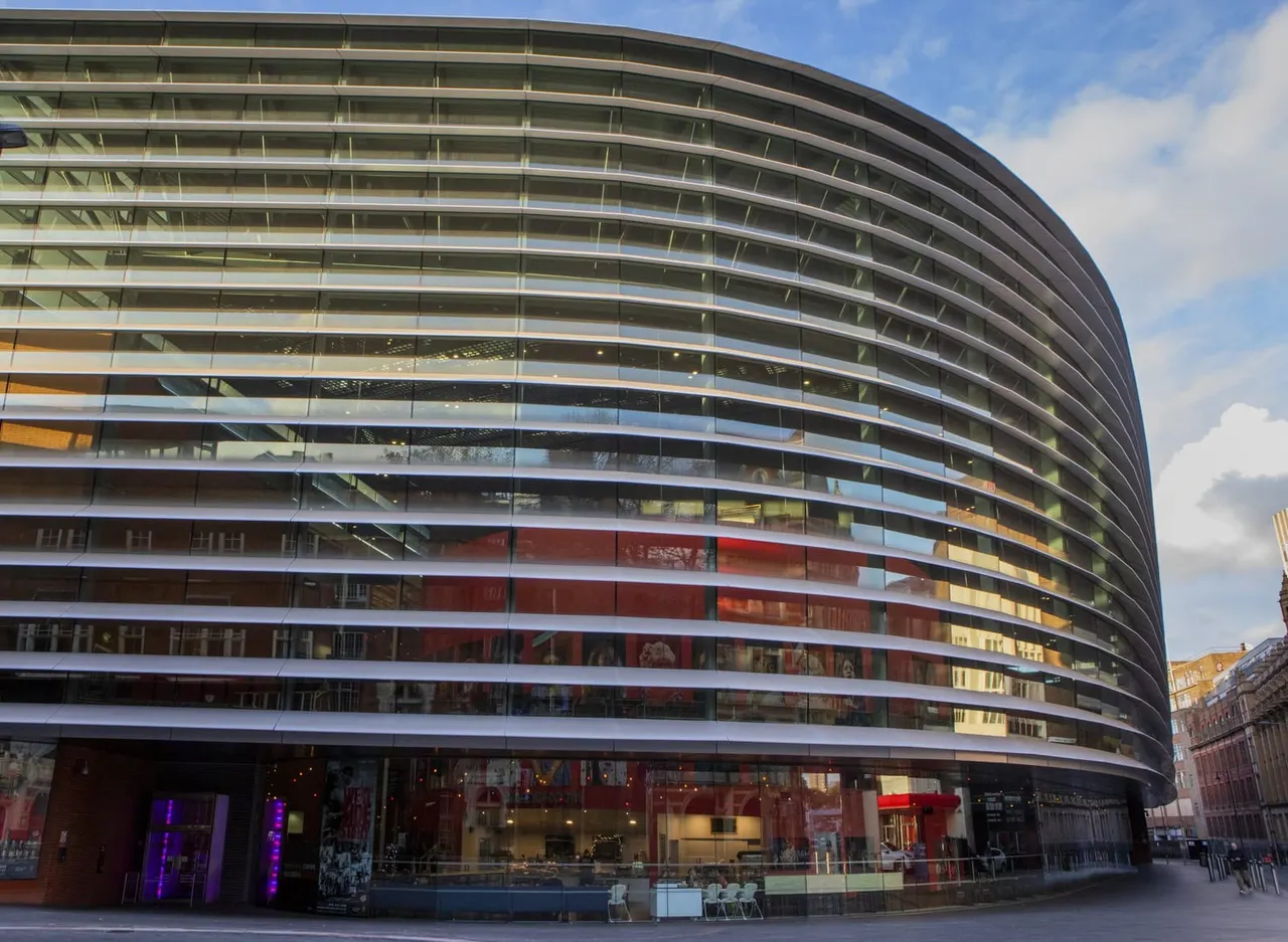 Modern curved building with horizontal striped glass facade and ground-level retail and entrance areas.