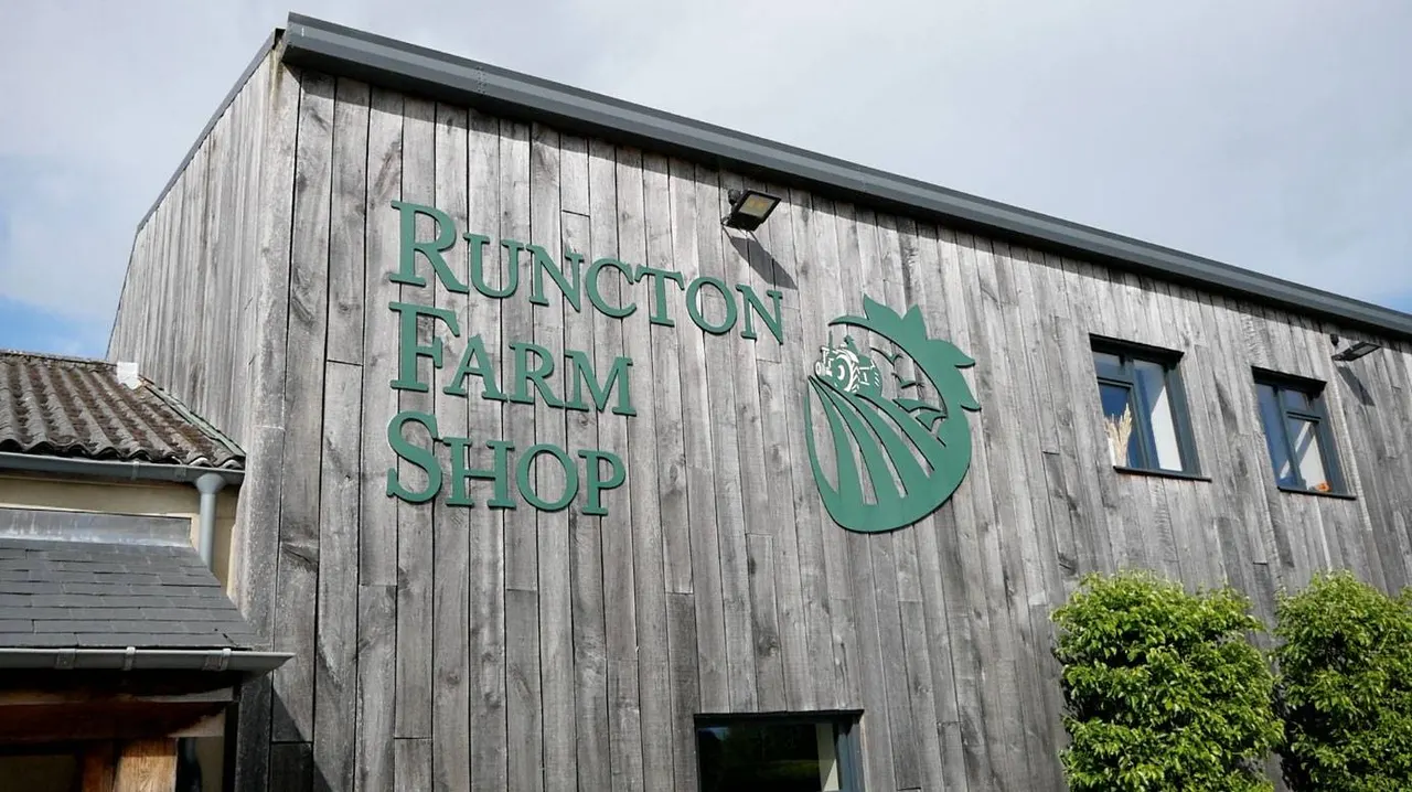 Exterior of a modern weathered wooden building with green signage reading "Runcton Farm Shop" and a farm logo.