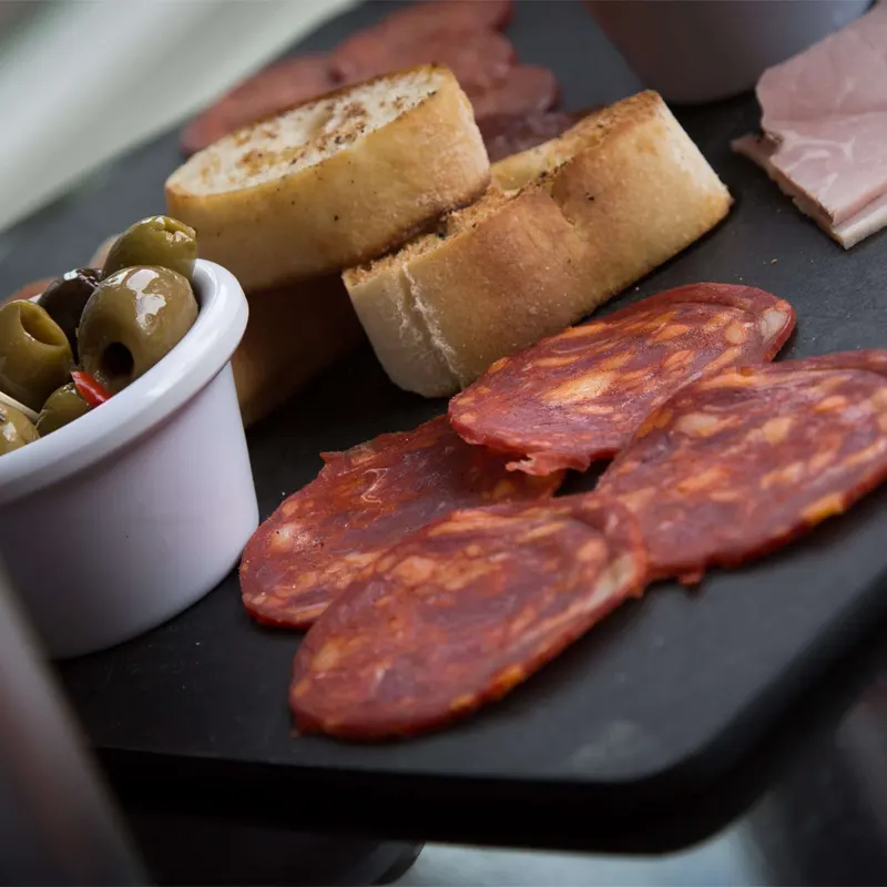 Charcuterie board with cured meats, olives in a small bowl, toasted bread slices and ham on a slate platter.