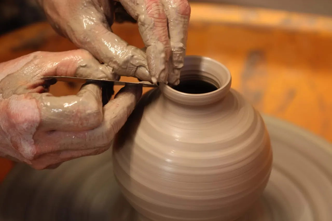Potter's hands shaping wet clay on a spinning wheel during a pottery class.