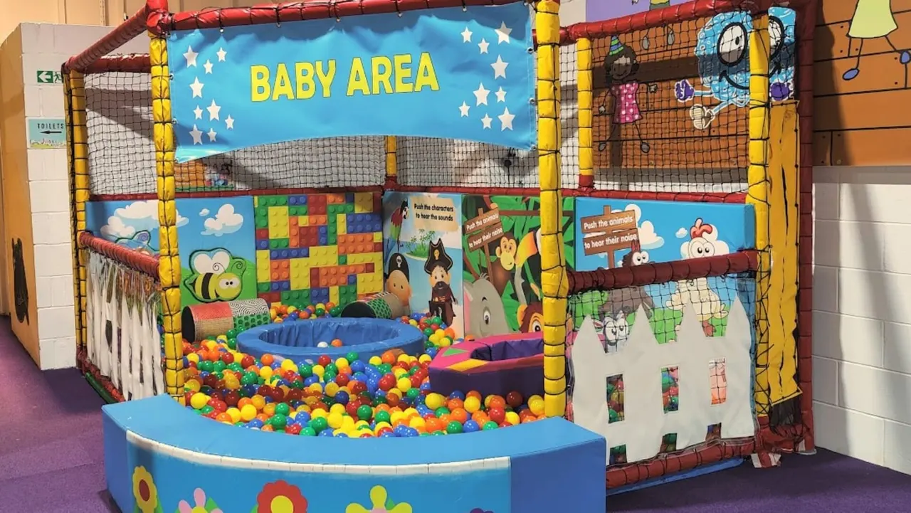 Colourful inflatable baby play area with ball pit containing multicoloured balls, decorated with cartoon characters and educational graphics.