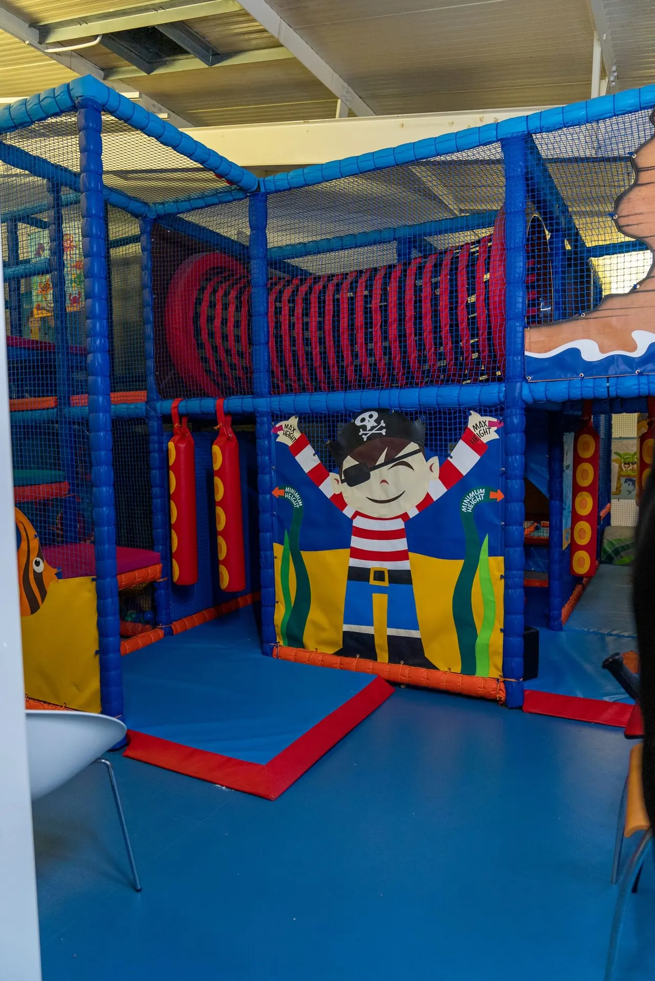 Pirate-themed soft-play frame with blue padding, red hanging bags and pirate height-chart panel