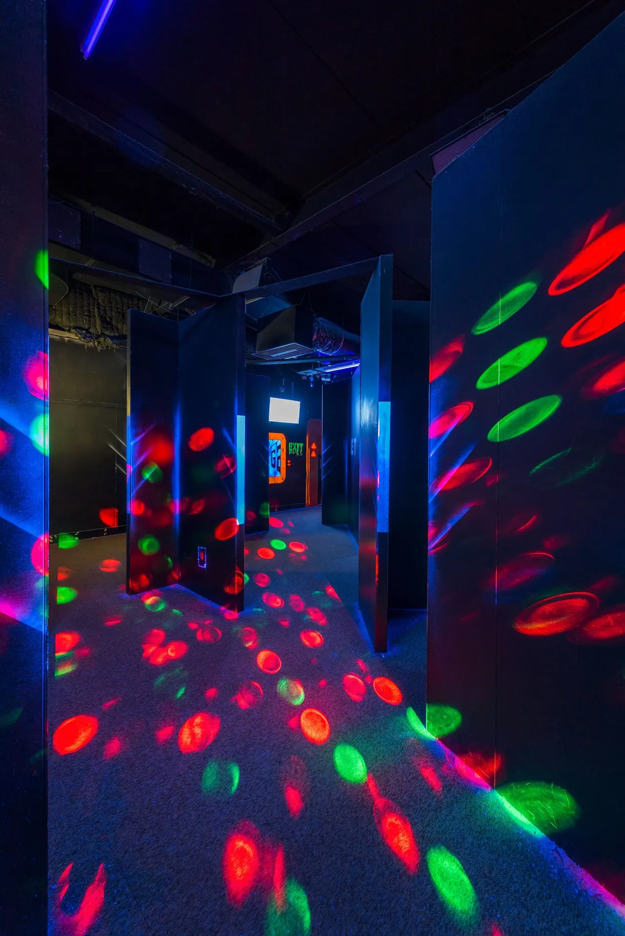 Interior of a neon-lit arcade or gaming space with bright red, green and blue glowing projections on walls and floor.