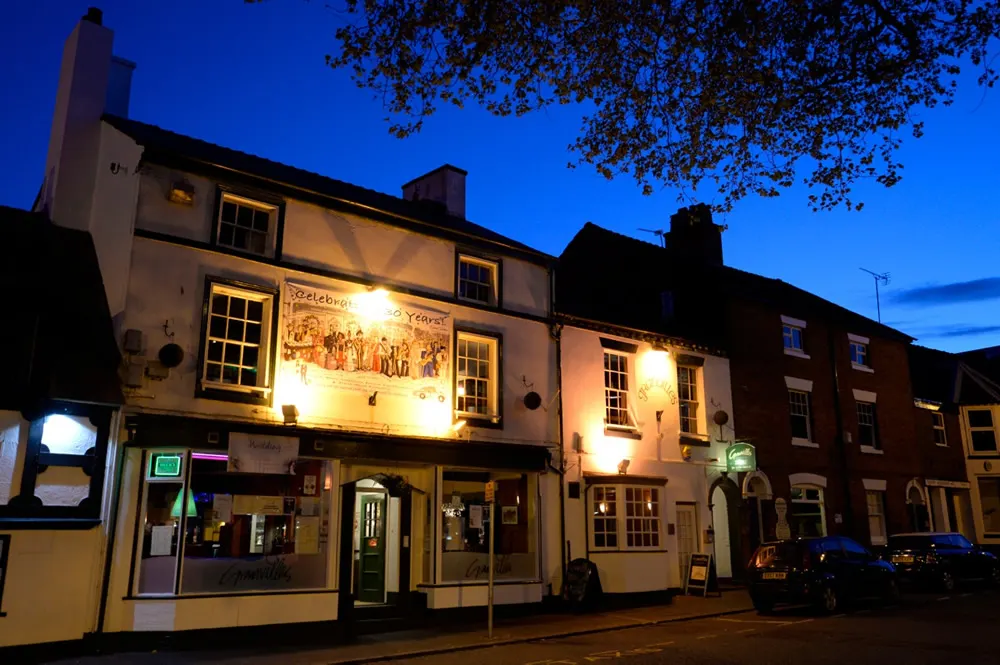 Historic building with illuminated pub or restaurant frontage at dusk, featuring cream and brick facades with lit windows.