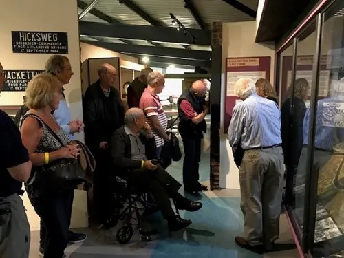 A group of visitors, including an elderly person in a wheelchair, gathered inside a museum exhibition space with display cases.