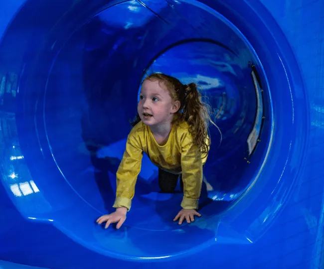 Young child crawling through a bright blue tunnel at an indoor play facility.