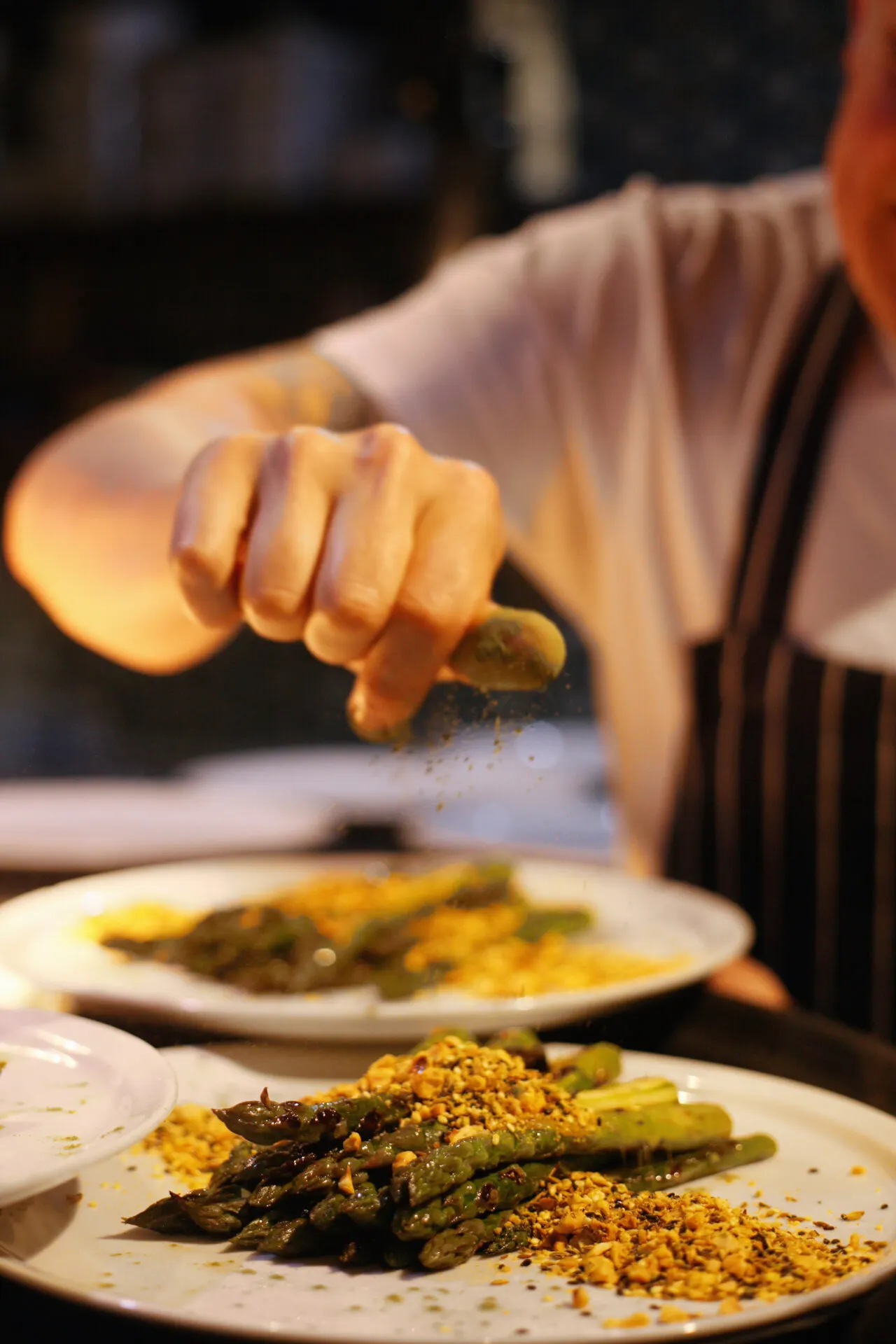Person squeezing lemon over asparagus and other vegetables on a plate during a dining experience.