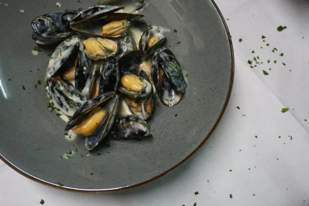 Cooked mussels with golden flesh and dark shells garnished with parsley on a grey plate.