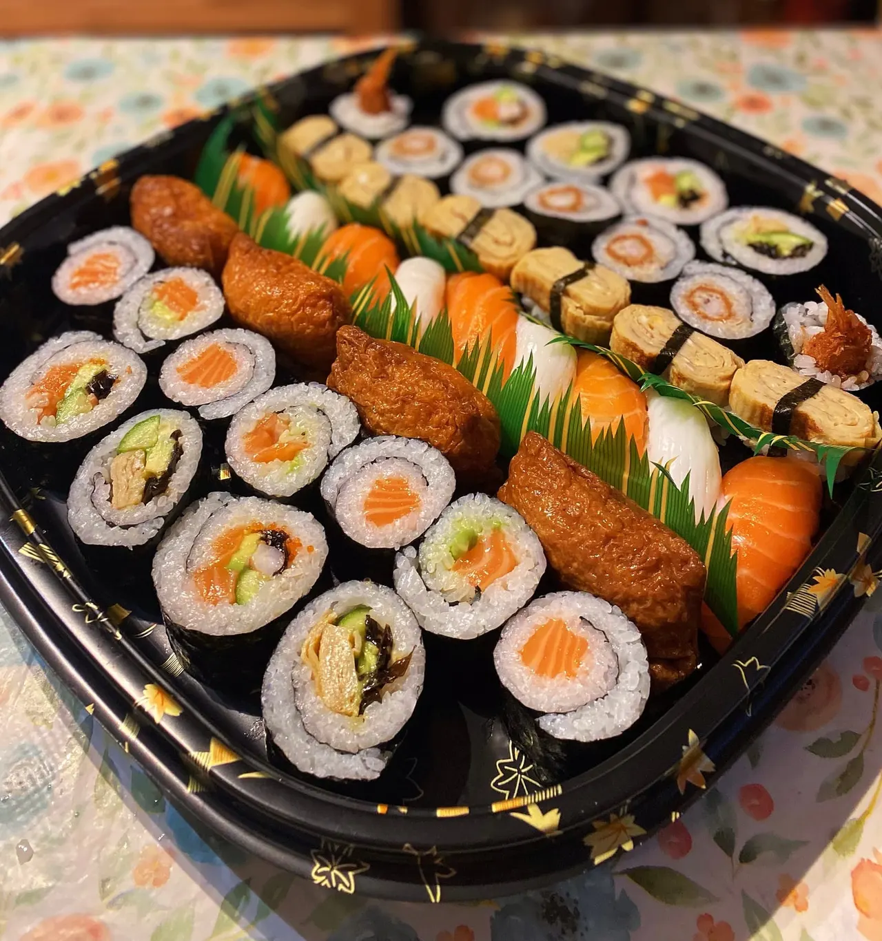 Assorted sushi platter with maki rolls, nigiri, and fried items arranged on a black tray.