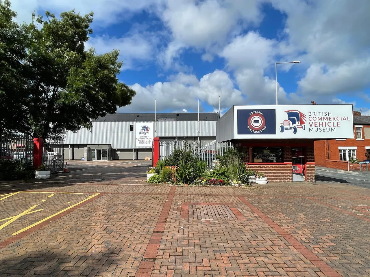 Exterior of the British Commercial Vehicle Museum building with signage, brick paving, and entrance forecourt under blue sky.