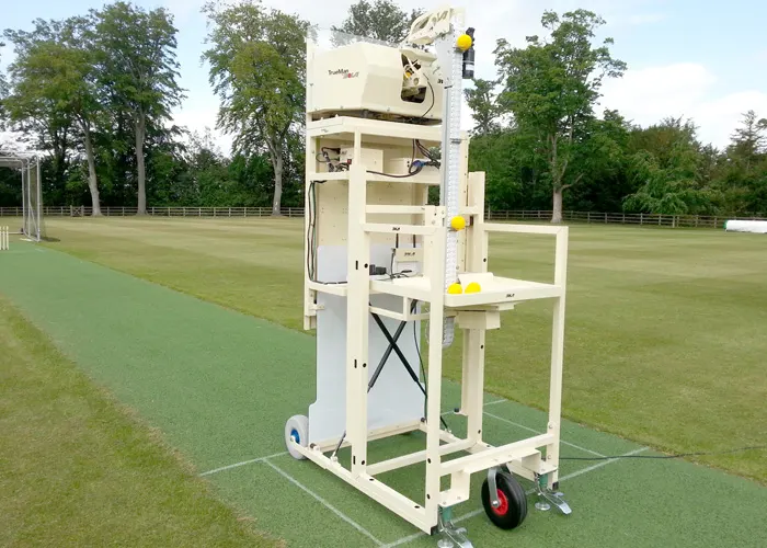 A ball-throwing machine mounted on a white mobile frame positioned on a grass pitch.
