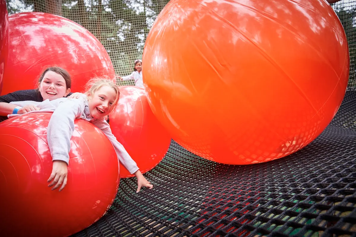 Two young children playing on large red inflatable balls in a bouncy castle activity area.