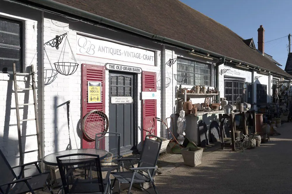 Antiques and vintage shops with white-painted buildings and red shutters displaying outdoor furniture and decorative items.