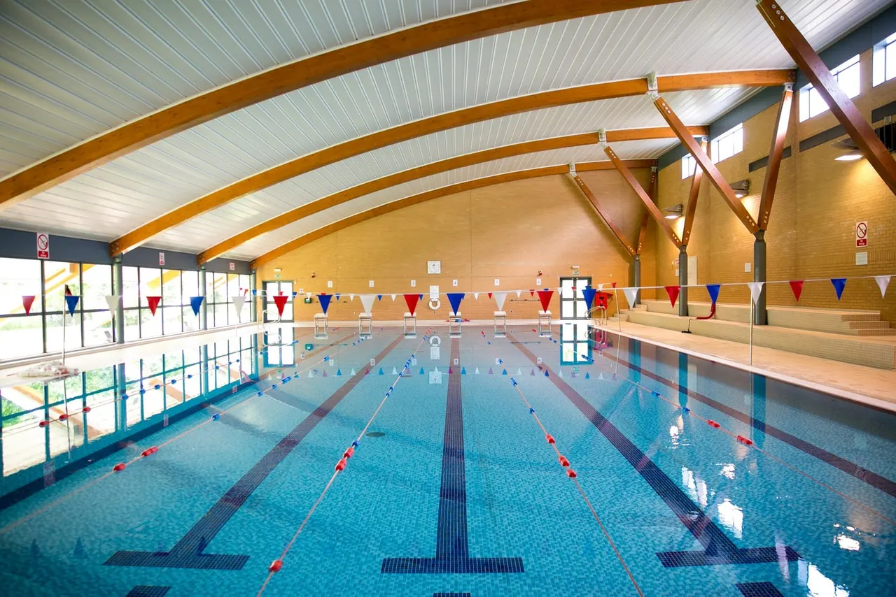Indoor swimming pool with multiple lanes marked by red and white dividers, decorative bunting overhead, and wooden arched ceiling beams.