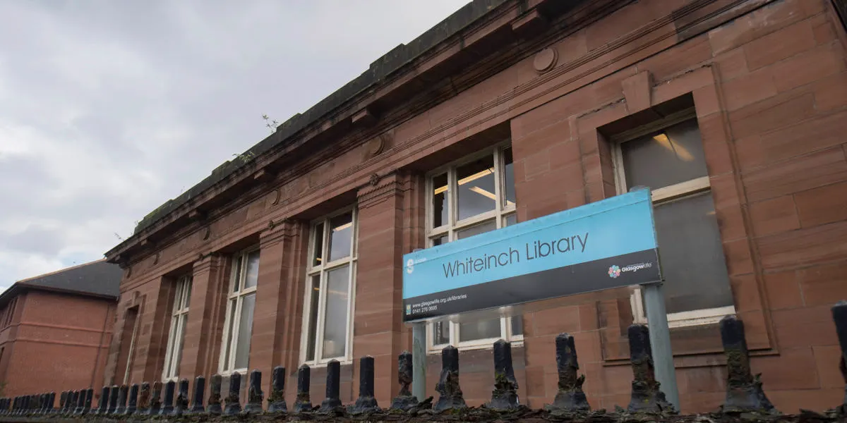 Red sandstone library building with blue signage, bollards along the front, and large windows.