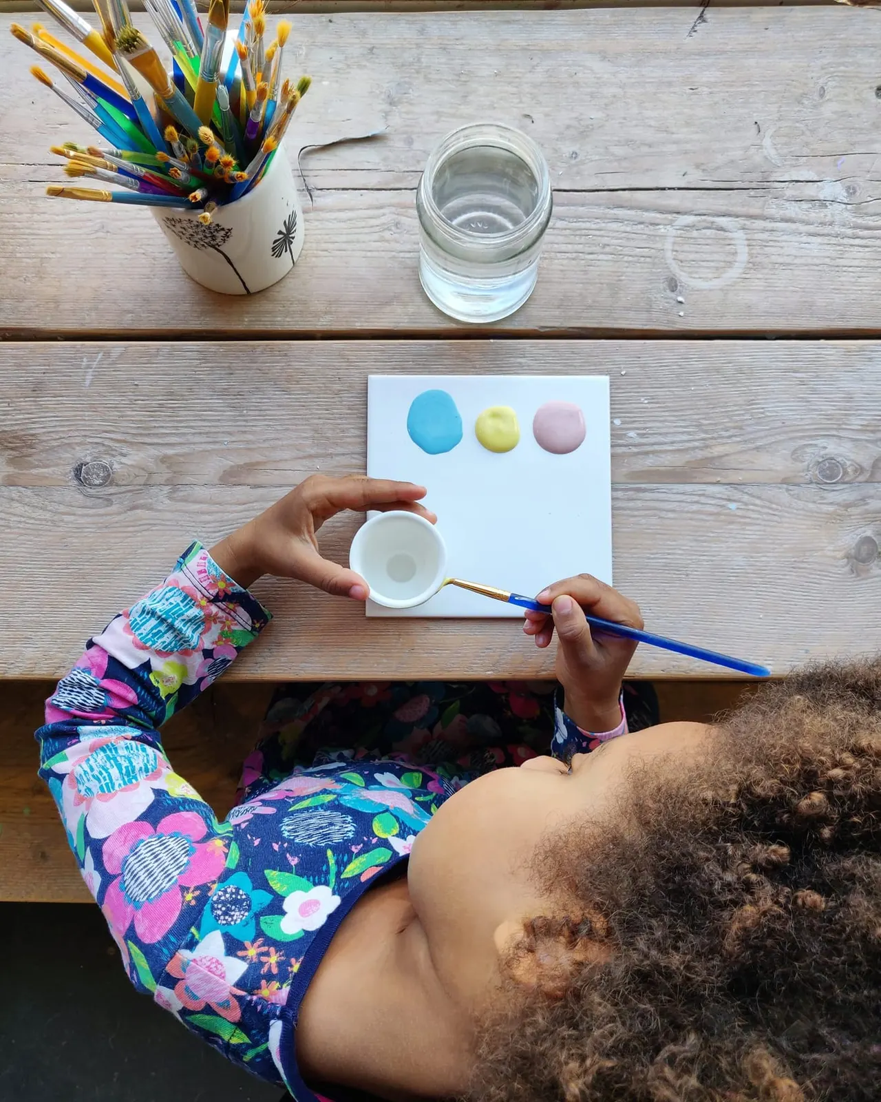 Child painting with watercolours at a wooden table during an art activity session.