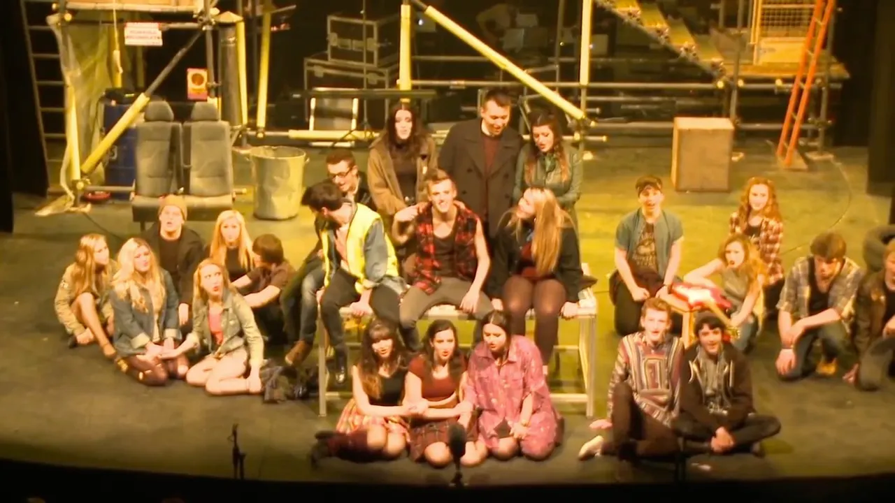 Large group of young people gathered on an industrial rooftop at night, sitting and standing together.