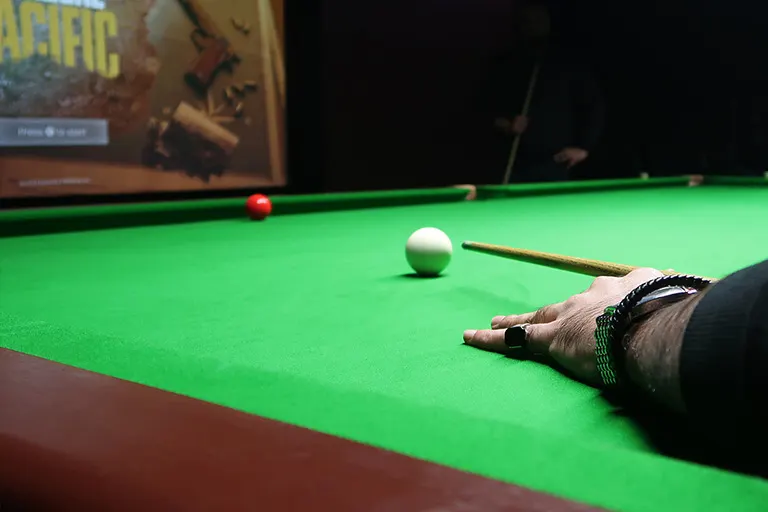 A snooker player's hand and cue on the green baize table with white and red balls during play.