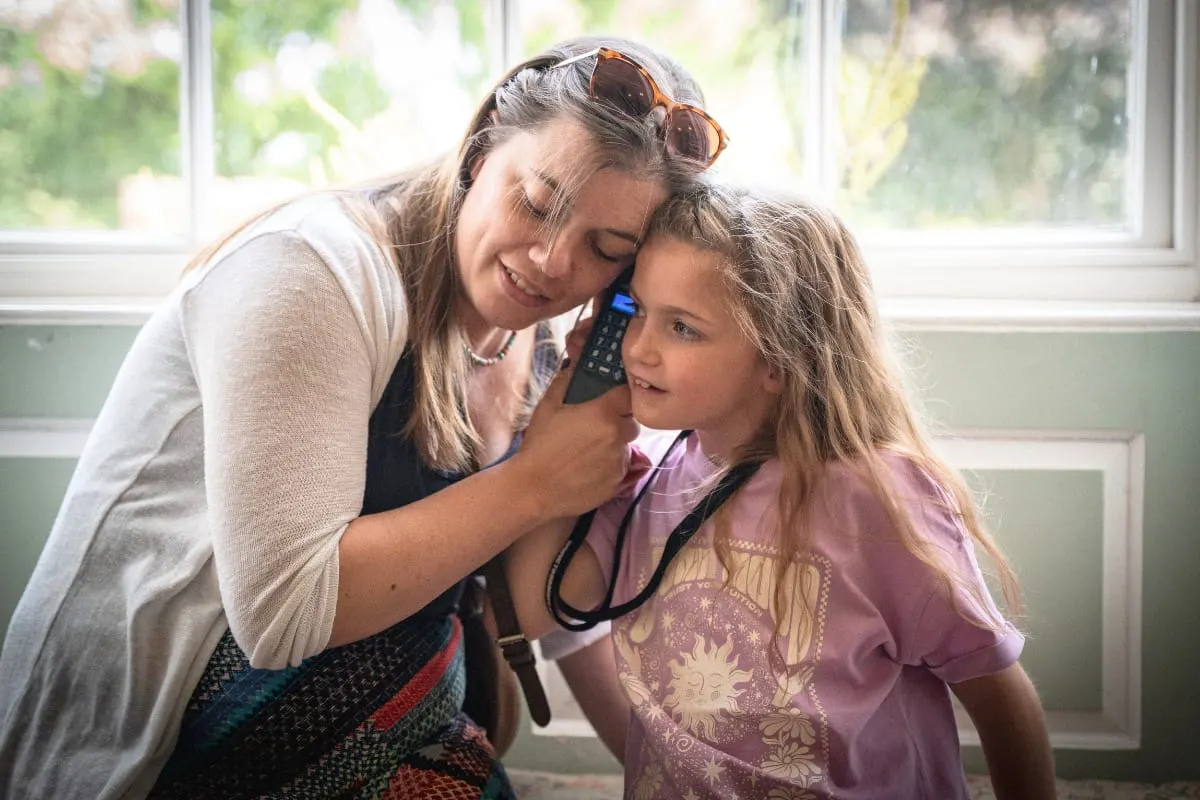 Woman using a stethoscope to examine a young girl indoors by a window.