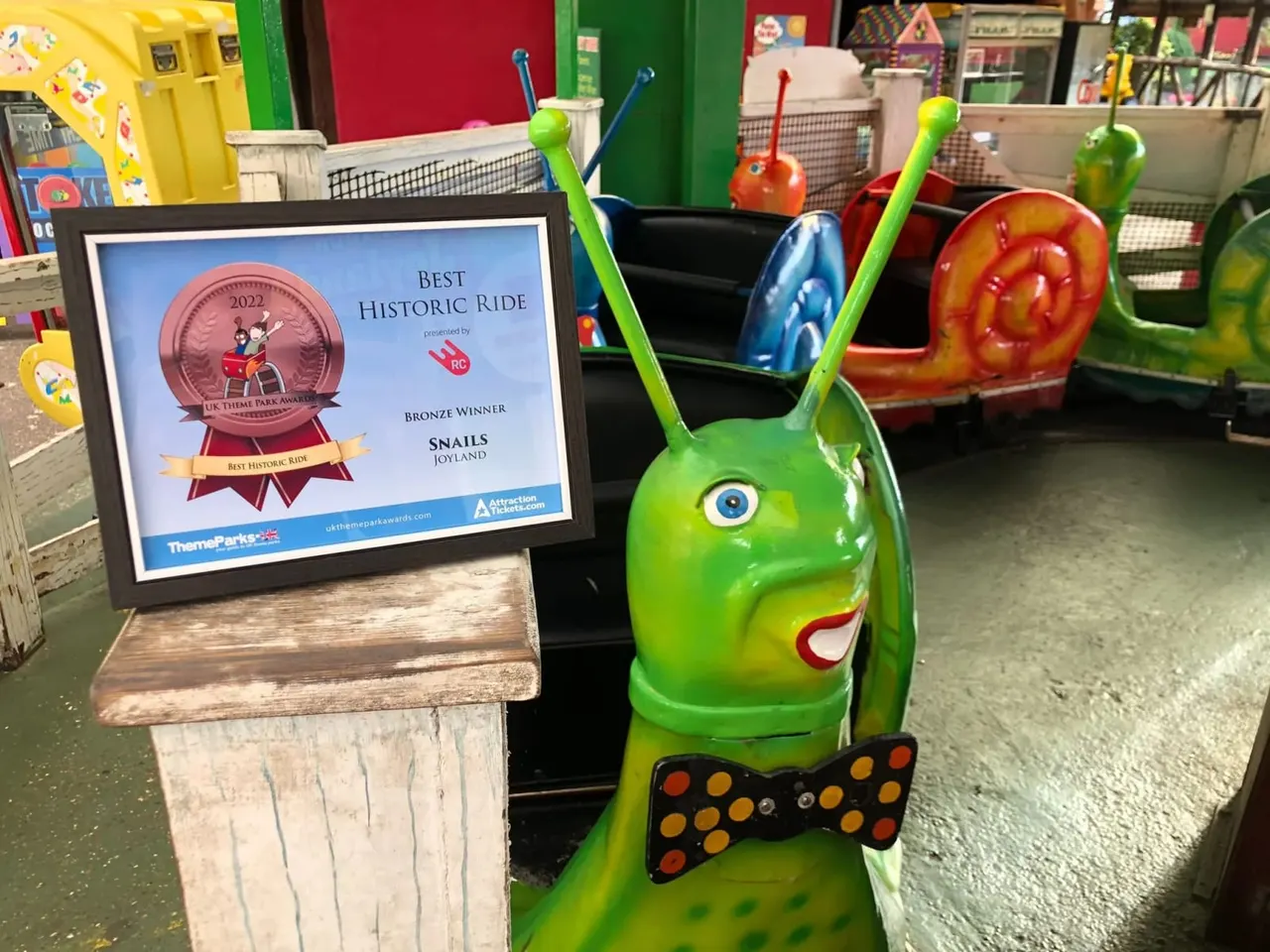 Colourful snail-themed children's fairground ride with award plaque displayed alongside it.