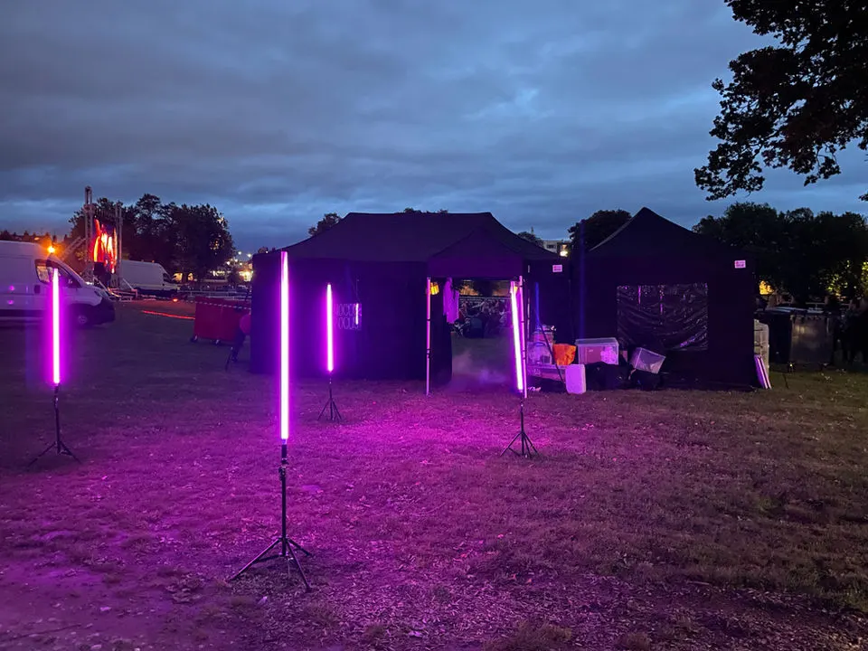 Outdoor cinema venue at dusk with purple neon-lit structures and seating areas set up on a grass field.