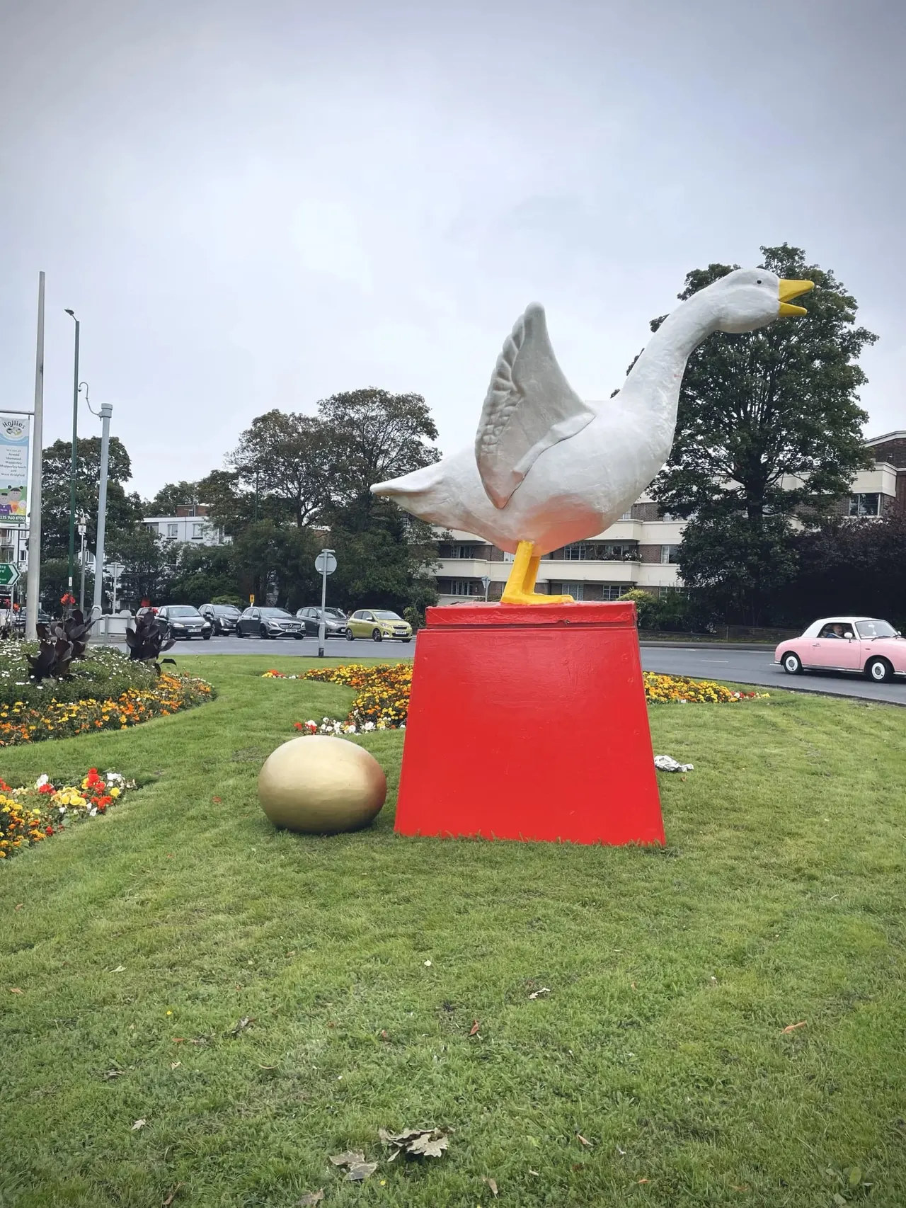 Large white seagull sculpture on a red plinth in a garden area beside a busy road.