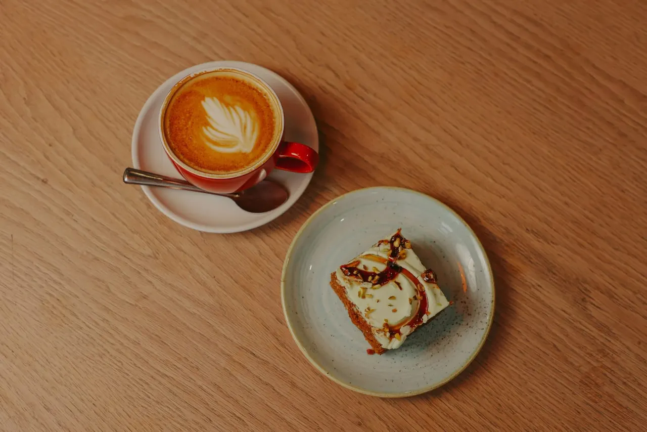 Overhead view of a cappuccino with latte art and a slice of toast with cheese on a wooden table.