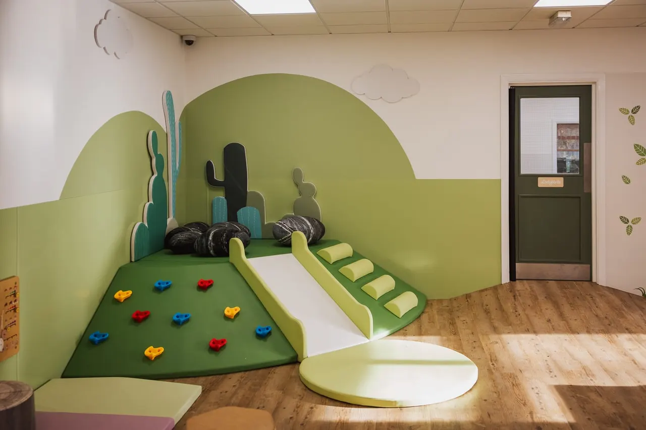 Children's play area with green desert-themed soft play structure featuring slides, climbing holds and cactus decorations.