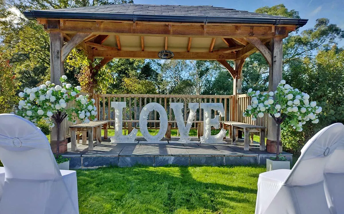 Wooden pavilion decorated with large "LOVE" letters and white hydrangea flowers for an outdoor wedding ceremony.