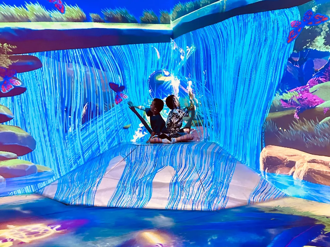 Two children exploring an interactive blue tunnel with colourful underwater-themed projections and animated fish surrounding them.