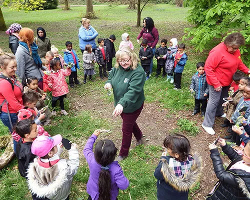 A group of children and adults gathered in a circle on a woodland path during an outdoor activity or guided tour.