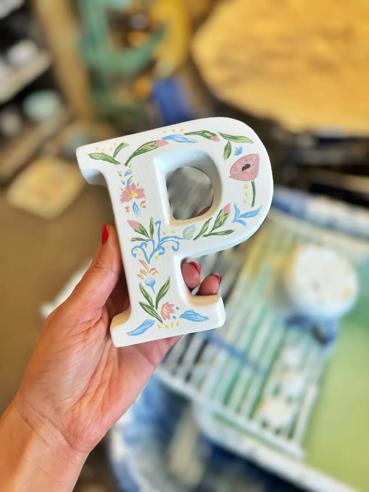 Person holding a hand-painted white ceramic letter P decorated with colourful floral motifs.