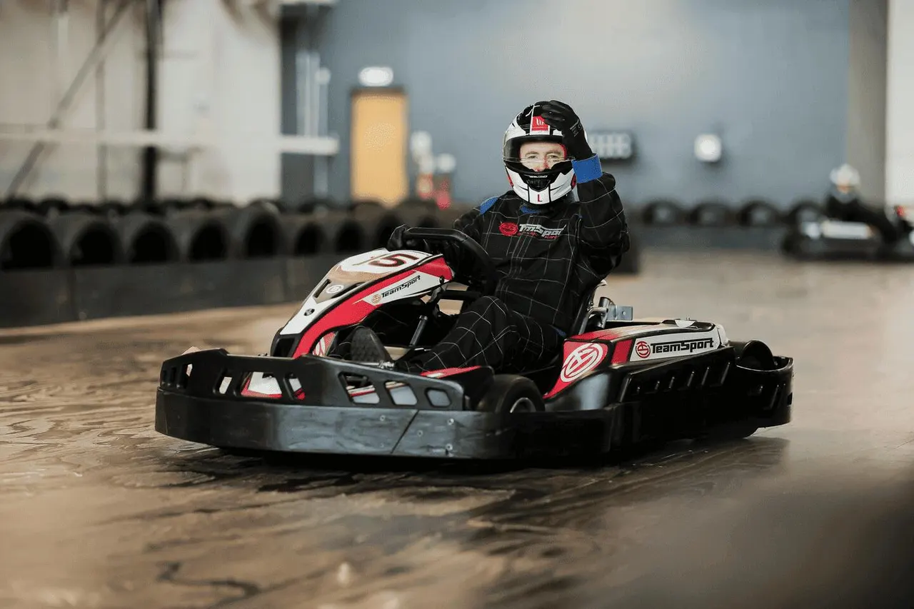 Person in racing helmet and black suit driving red and black go-kart on indoor track with tyres lining the course.