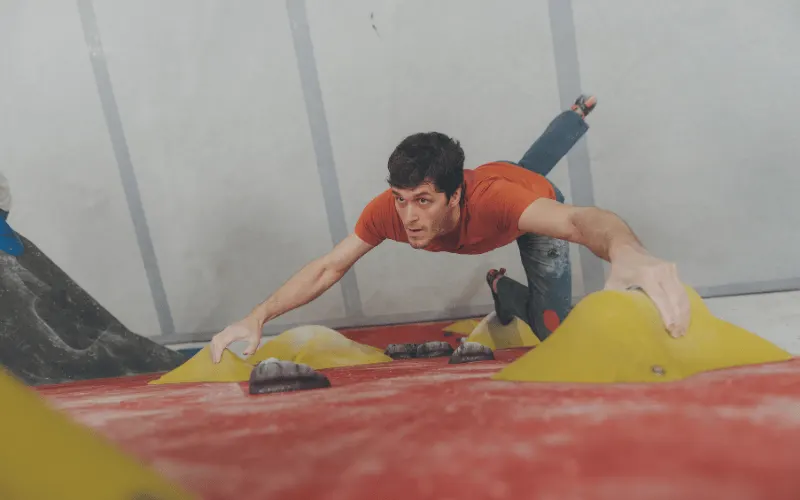 Man climbing an indoor climbing wall with yellow and red handholds.