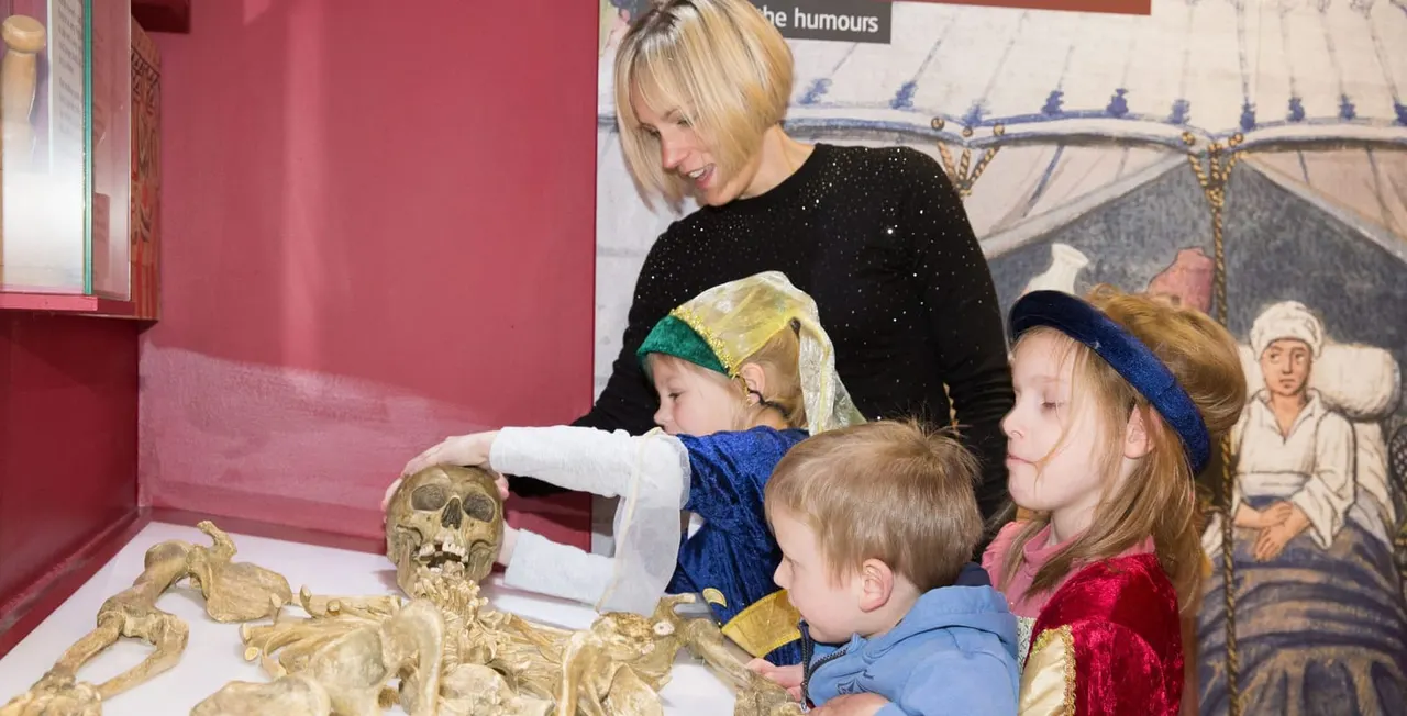 Adult and three children examining a skeletal display in a museum case with pink walls.