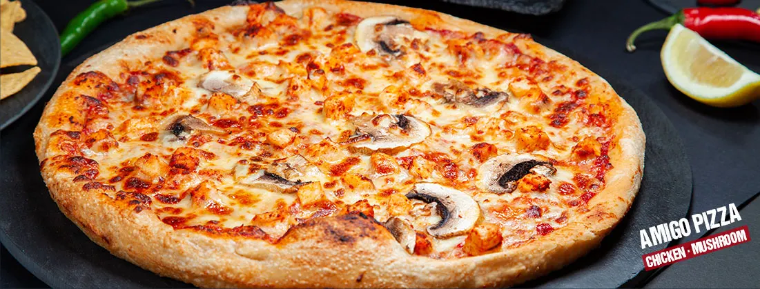A freshly baked pizza topped with melted cheese, chicken, mushrooms and tomato sauce, garnished with green chilli and lemon wedge.