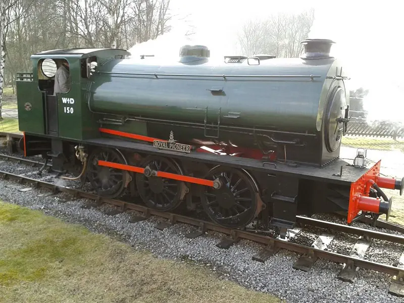 Stationary heritage steam locomotive with green cab and black boiler on railway tracks.