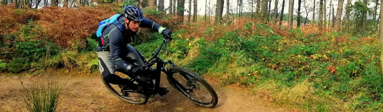 Mountain biker riding on a dirt trail through a woodland forest in autumn.