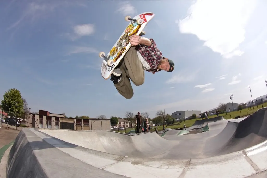 Skateboarder performing a trick mid-air above concrete bowl at outdoor skatepark.