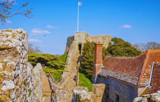 Stone castle ruins with moss-covered walls, a tower flying the Canadian flag, and red-tiled buildings on a green hillside.