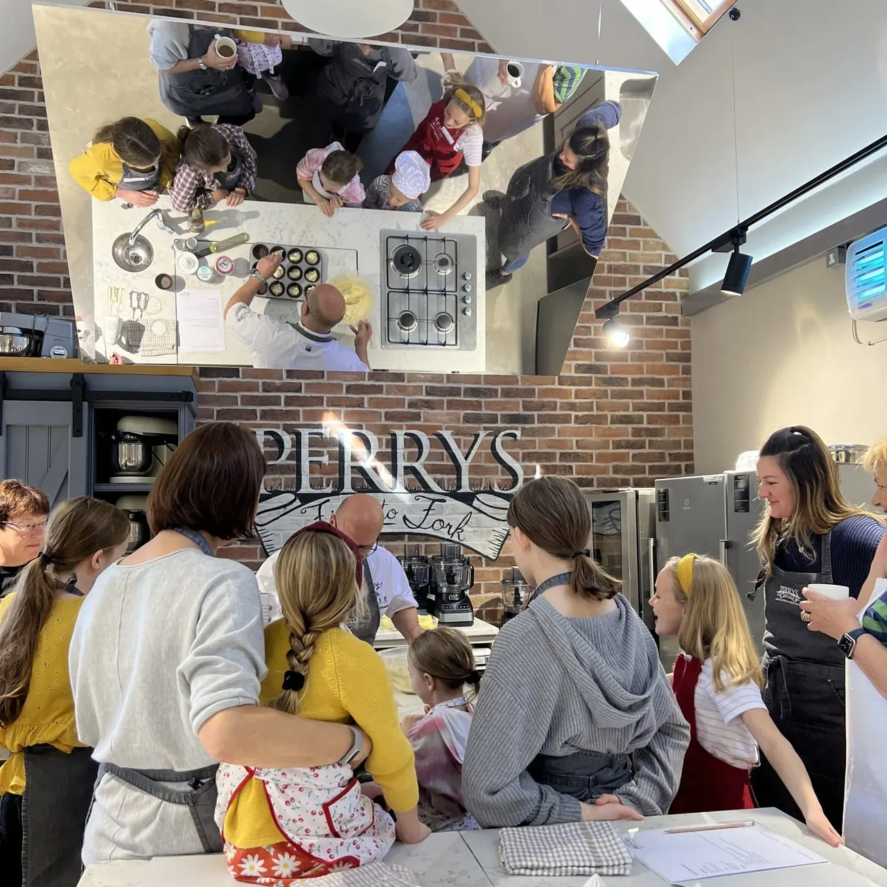 Overhead view of visitors and staff participating in a cooking class at a kitchen venue with brick walls.