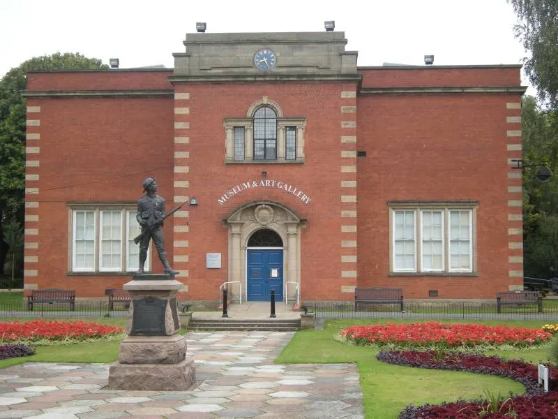 Red brick museum building with a statue in the foreground and flower beds on either side of the entrance.