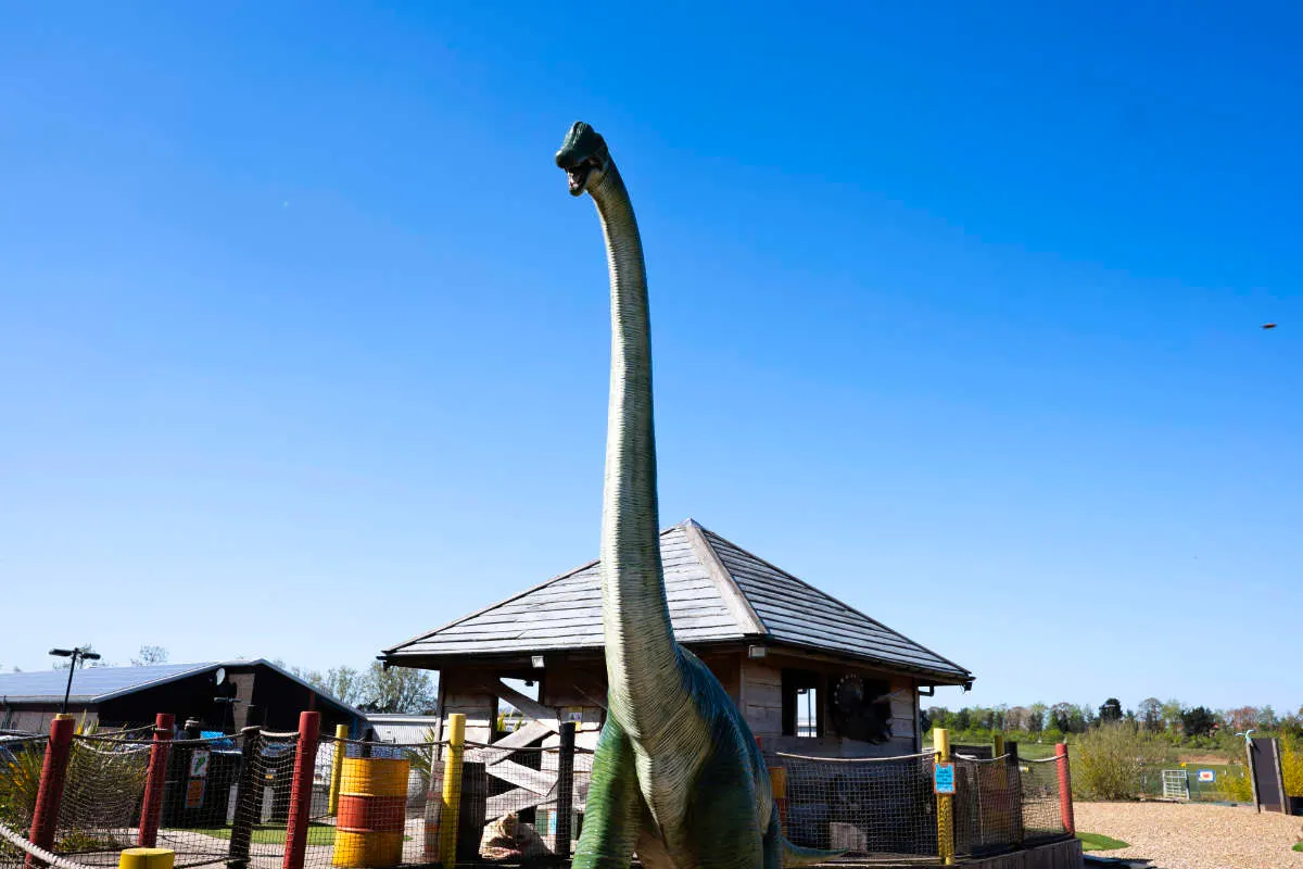 Giant dinosaur model with long neck towering over a themed golf course building against clear blue sky.