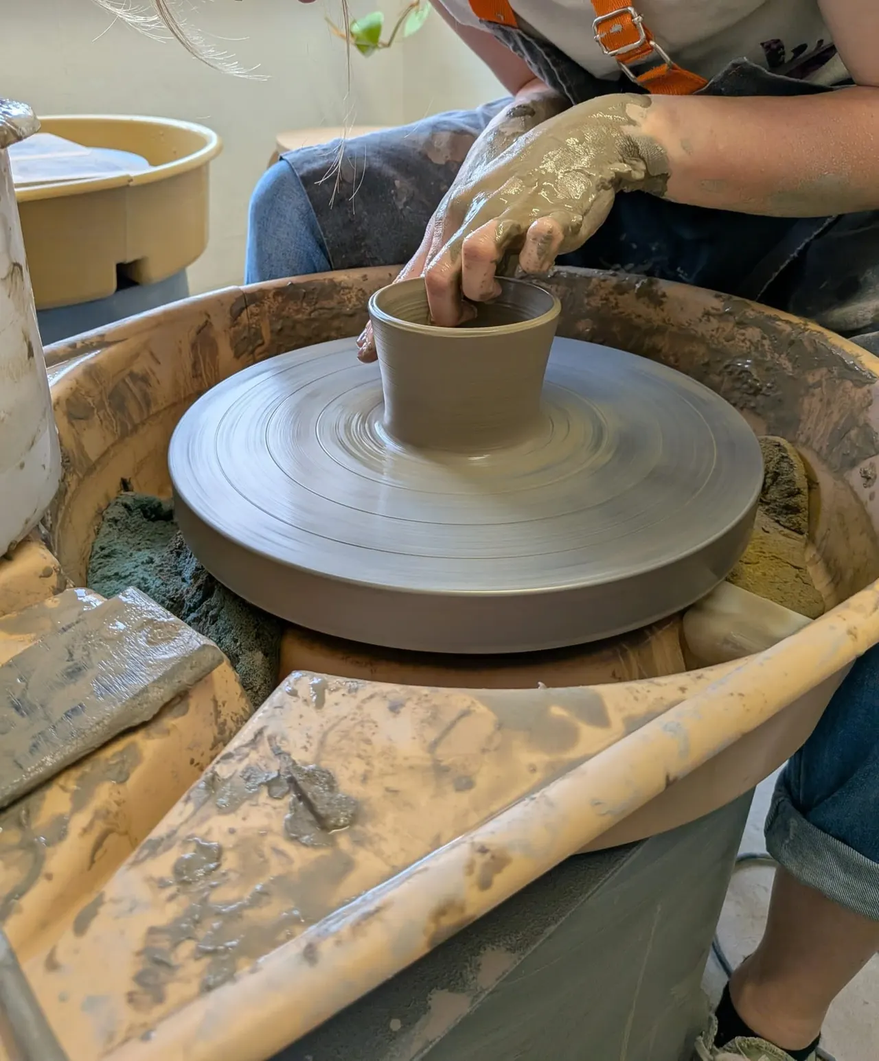 Person shaping clay on a pottery wheel during a ceramics workshop.