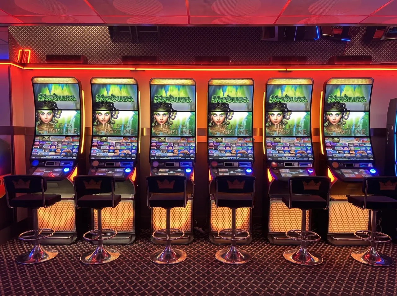 Row of six illuminated slot machines with Medusa-themed displays in a gaming venue with red neon lighting.