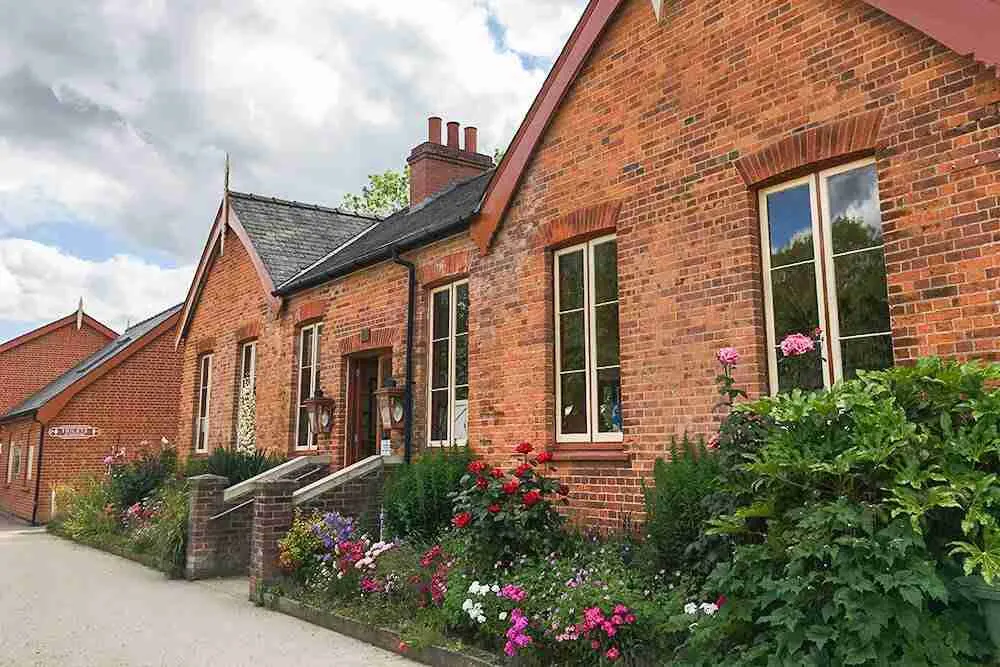 Victorian brick station building with flowering borders and shrubs along the front pathway.