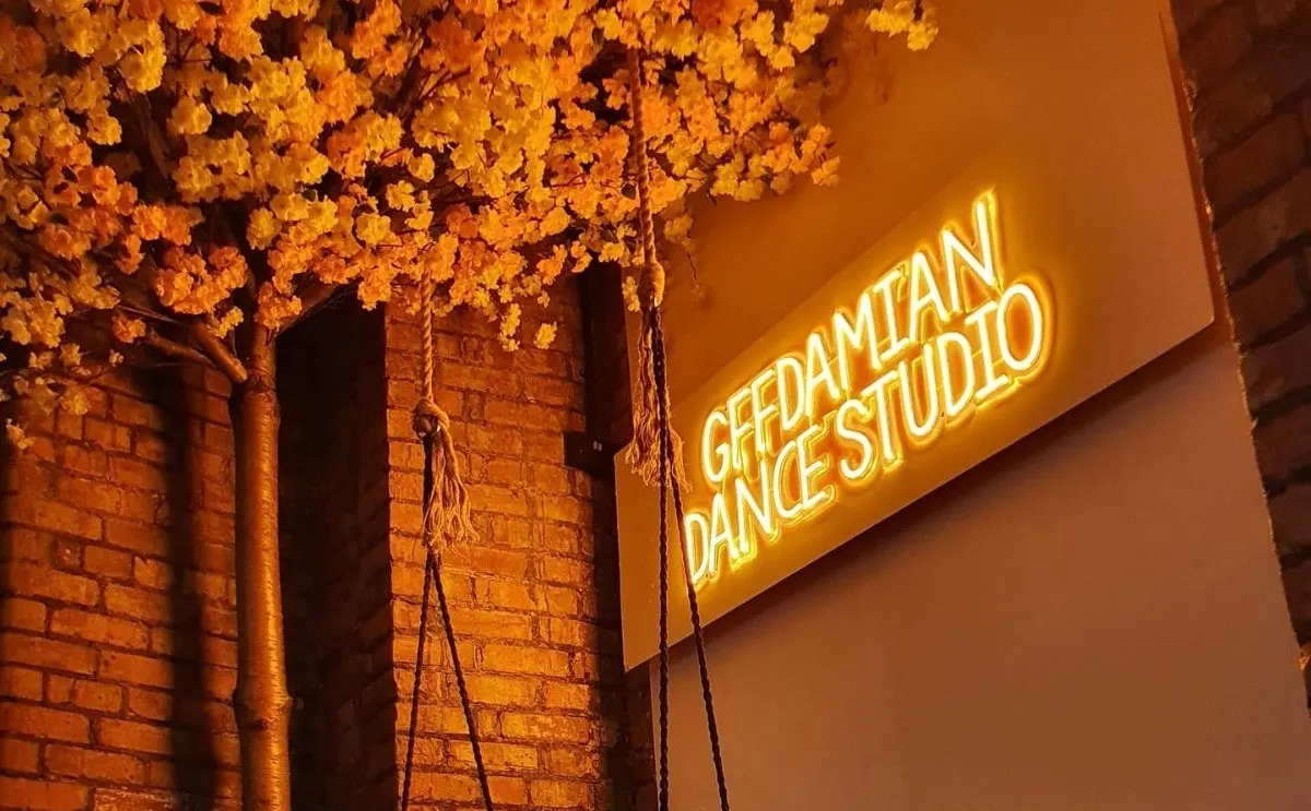 Neon sign for a dance studio with golden hanging flowers decorating a brick wall entrance.