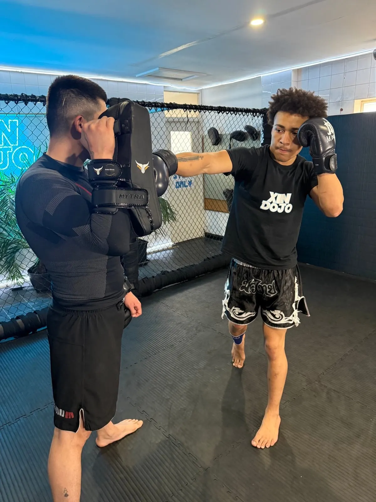 Two young men sparring with boxing gloves in a gym ring, one throwing a punch whilst the other defends.