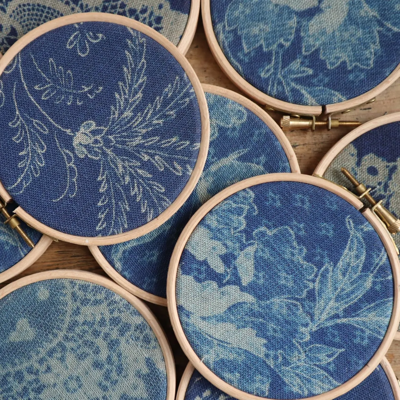 Embroidery hoops with blue linen featuring delicate leaf designs in cream thread.